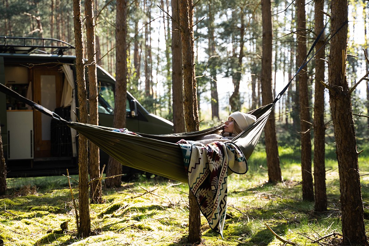 vrouw in hangmat in het bos met campervan op de achtergrond