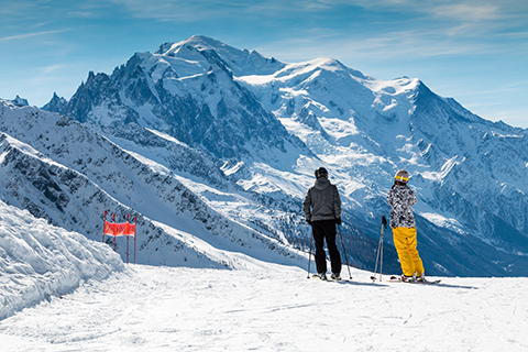 Skiers standing on a ski slope looking across to Mont Blanc in winter.  The male and female are wearing bright ski clothes.