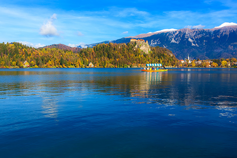 Panorama of Lake Bled Blejsko Jezero, Slovenis with boat and autumn colorful Julian Alps in background